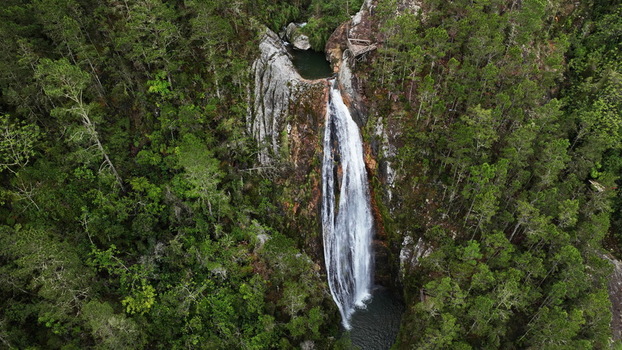 Aerial view of Salto de Aguas Blancas waterfall cascading down rocky cliffs surrounded by dense pine forests in the mountains of Constanza La Vega Province Dominican Republic.