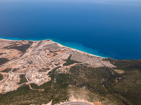 Aerial view of the turquoise coastline and modern residential developments nestled between green hills and the deep blue sea in Palase Vlore County Albania.