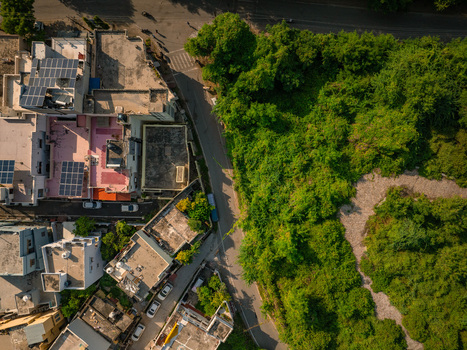 Aerial view of residential rooftops equipped with solar panels alongside a road and dense green vegetation in Udaipur Rajasthan India.