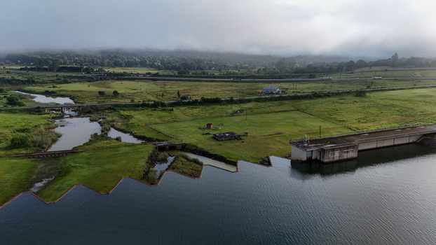 Aerial view of Midmar Dam wall with green fields a winding river and misty hills under an overcast sky in Howick KwaZulu Natal South Africa. Aerial view of Midmar Dam wall with green fields a winding river and misty hills under an overcast sky in Howick KwaZulu Natal South Africa.