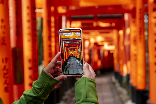 View of a person holding a smartphone to capture the vibrant orange Senbon Torii Thousand Torii Gates at Fushimi Inari taisha shrine in Kyoto Kyoto Japan.