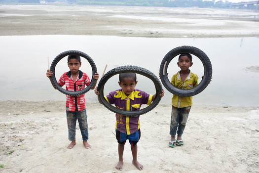 Kushtia Khulna Division Bangladesh 12 March 2020 View of three young boys standing on a riverbank each holding a bicycle tire as a playful frame. Kushtia Khulna Division Bangladesh 12 March 2020 View of three young boys standing on a riverbank each holding a bicycle tire as a playful frame.