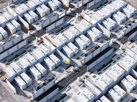 Aerial view of a large scale battery energy storage system facility with rows of white containers separated by concrete walls and paved access roads in Poland.