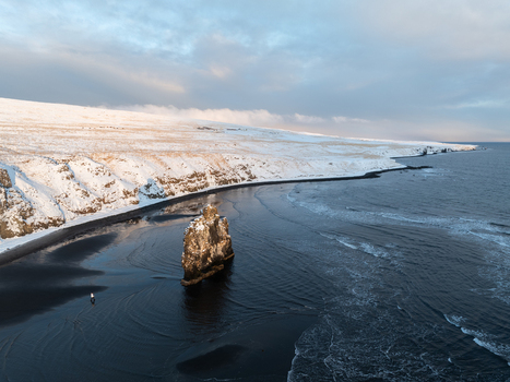 Aerial view of the Hvitserkur rock formation standing on a black sand beach along the snow covered coastline of Iceland. Aerial view of the Hvitserkur rock formation standing on a black sand beach along the snow covered coastline of Iceland.
