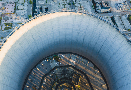 Aerial view of a massive concrete cooling tower at an industrial power plant revealing its circular structure support columns and dramatic engineering design in Italy. Aerial view of a massive concrete cooling tower at an industrial power plant revealing its circular structure support columns and dramatic engineering design in Italy.
