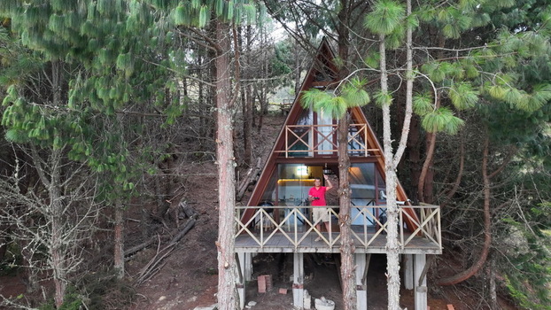Aerial view of a wooden A frame cabin at Corani nestled in a pine forest with a person standing on the balcony in Cochabamba Departamento de Cocha Bolivia.