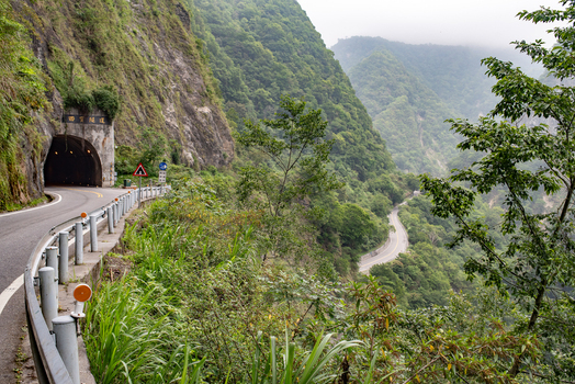 View of the winding road leading into a tunnel within the lush mountainous landscape of Taroko National Park in Xiulin Township Hualien County Taiwan.
