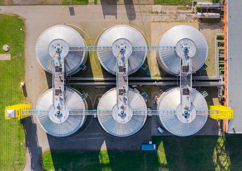 Aerial view of a waste water treatment plant featuring six large circular metal tanks connected by industrial walkways surrounded by green grass in Poland. Aerial view of a waste water treatment plant featuring six large circular metal tanks connected by industrial walkways surrounded by green grass in Poland.