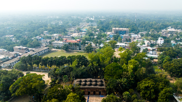 Aerial view of Bagha Shahi Mosque with its historic terracotta domes surrounded by lush greenery and urban buildings in Rajshahi Rajshahi Division Bangladesh.