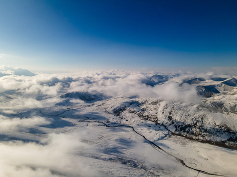 Aerial view of Babusar Pass with snow covered mountain peaks and a winding road under a clear blue sky and thick white clouds Babusar KPK Pakistan.