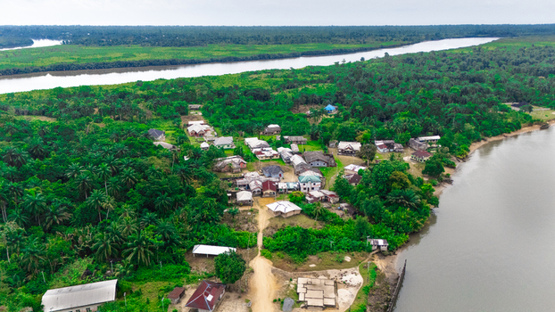 Aerial view of a small village nestled among dense tropical vegetation and palm trees along the banks of a winding river in Minima Rivers Nigeria.