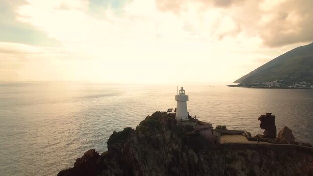 Aerial view of lighthouse on a rocky cliff at sunset Italy.