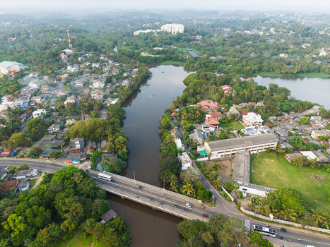 Aerial view of a river flowing through lush tropical vegetation and residential buildings with a bridge crossing the water in Galle Southern Province Sri Lanka.