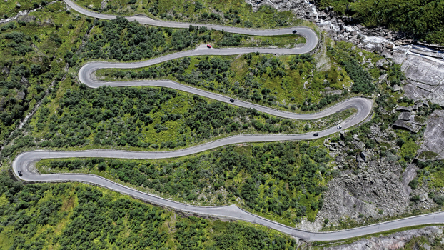 Aerial view of a winding mountain road with sharp hairpin turns surrounded by lush green vegetation and rocky terrain in Nordland Norway. Aerial view of a winding mountain road with sharp hairpin turns surrounded by lush green vegetation and rocky terrain in Nordland Norway.