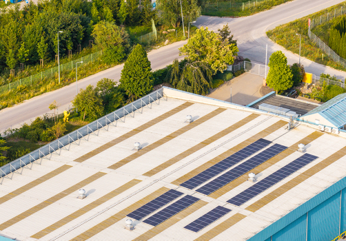 Aerial view of solar panels installed on a flat industrial building roof surrounded by green trees and a paved road in Kowale Pomeranian Voivodeship Poland. Aerial view of solar panels installed on a flat industrial building roof surrounded by green trees and a paved road in Kowale Pomeranian Voivodeship Poland.