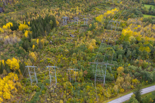 Aerial view of high voltage power lines and metal pylons stretching through a dense forest with vibrant autumn foliage and a road nearby in Andalsnes More og Romsdal Norway. Aerial view of high voltage power lines and metal pylons stretching through a dense forest with vibrant autumn foliage and a road nearby in Andalsnes More og Romsdal Norway.