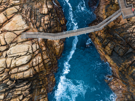 Aerial view of the wooden footbridge at Canal Rocks spanning the rugged dark rock formations with crashing blue ocean waves below in Yallingup Western Australia Australia.
