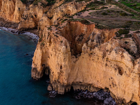 Aerial view of Ponta da Piedade featuring dramatic golden limestone cliffs sea caves and turquoise Atlantic waters along the coastline in Lagos Faro Portugal.