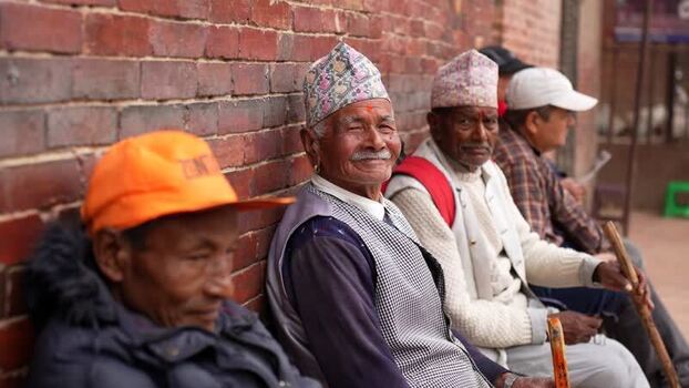 View of elderly Nepalese men sitting against a brick wall Nepal.