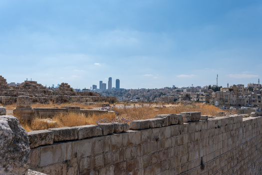 View of the historic Umayyad Palace ruins with dry grass and stone walls in the foreground overlooking the modern city skyline of Amman Amman Governorate Jordan.