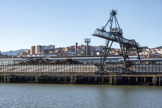View of a large blue industrial crane and piles of scrap metal at the port with the city skyline in the background Greater Bilbao Basque Country Spain. View of a large blue industrial crane and piles of scrap metal at the port with the city skyline in the background Greater Bilbao Basque Country Spain.