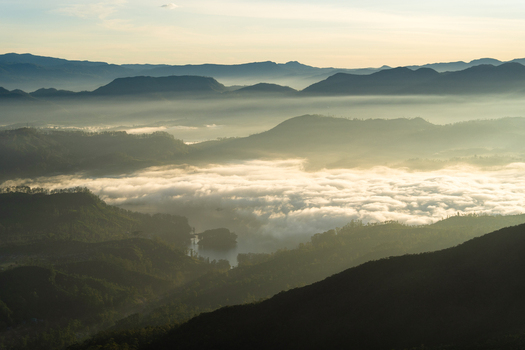 View of Adam s Peak and the surrounding mountain range covered in a thick layer of morning mist and golden sunlight in Ratnapura Sabaragamuwa Province Sri Lanka. View of Adam s Peak and the surrounding mountain range covered in a thick layer of morning mist and golden sunlight in Ratnapura Sabaragamuwa Province Sri Lanka.