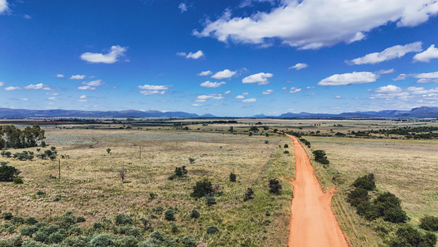 Aerial view of a long red dirt road stretching through the vast savanna landscape near Alma under a blue sky Waterberg District Municipality Limpopo South Africa. Aerial view of a long red dirt road stretching through the vast savanna landscape near Alma under a blue sky Waterberg District Municipality Limpopo South Africa.