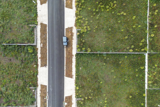 Kalkallo Australia 28 April 2026 Aerial view of a new residential development site with a paved road sidewalks vacant green lots and a parked vehicle with an open door.
