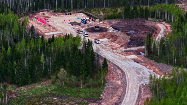 Aerial view of wind turbine foundation under construction in a forest clearing with trucks and heavy machinery surrounded by dense pine trees in Latvia. Aerial view of wind turbine foundation under construction in a forest clearing with trucks and heavy machinery surrounded by dense pine trees in Latvia.
