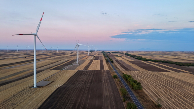 Aerial view of wind turbines standing in vast agricultural fields at sunset with a road running through the landscape in Vladimirovac Vojvodina Serbia.