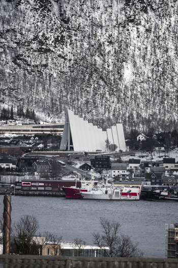 View of the Arctic Cathedral and harbor with ships against a snow covered mountain backdrop in Tromso Troms Norway.