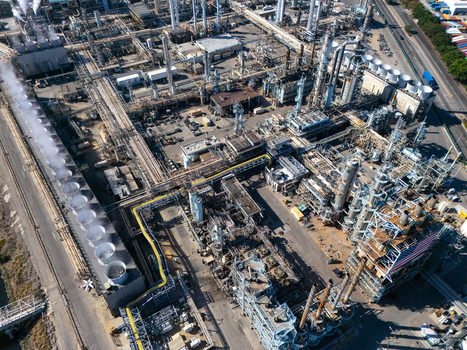 Aerial view of an oil refinery with industrial structures cooling towers pipelines and storage tanks in Carson California United States.