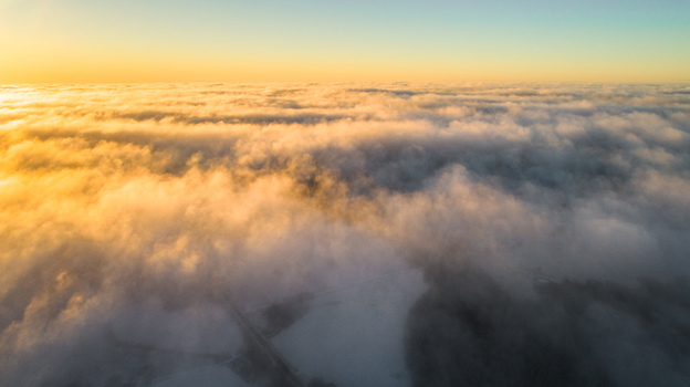 Aerial view of a thick layer of clouds illuminated by the golden light of sunset over the landscape of Latvia. Aerial view of a thick layer of clouds illuminated by the golden light of sunset over the landscape of Latvia.