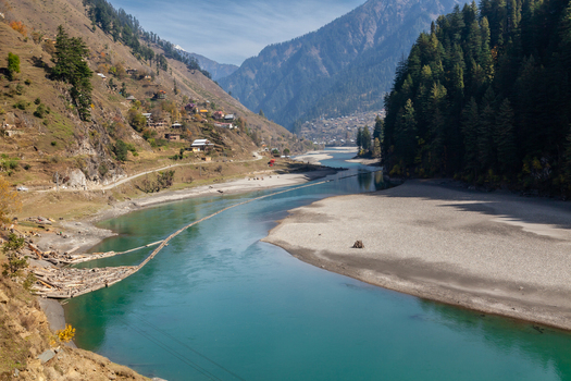 View of the turquoise Neelum River flowing through a deep valley surrounded by steep forested mountains and village houses in Arang Kel Azad Kashmir Pakistan. View of the turquoise Neelum River flowing through a deep valley surrounded by steep forested mountains and village houses in Arang Kel Azad Kashmir Pakistan.