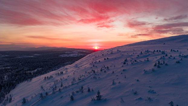 Aerial view of the snow covered slopes of Luosto fell under a vibrant pink sunset sky with dense pine forests Sodankyla Lapland Finland. Aerial view of the snow covered slopes of Luosto fell under a vibrant pink sunset sky with dense pine forests Sodankyla Lapland Finland.