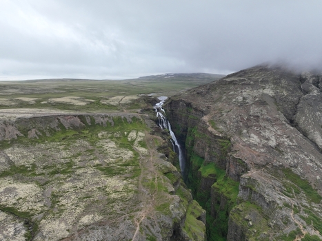 Aerial view of Glymur Waterfall cascading through a deep mossy canyon surrounded by rugged volcanic terrain under a cloudy sky in Bifrost Borgarbyggd Iceland.