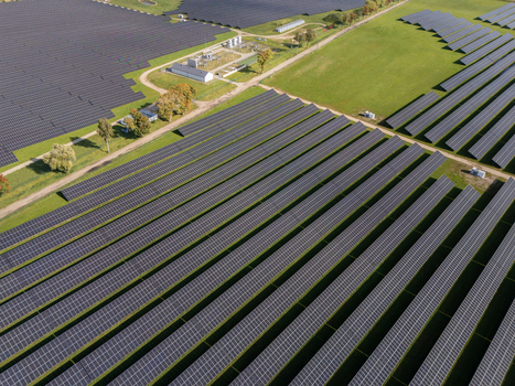 Aerial view of a large solar farm with rows of photovoltaic panels installed on green fields in Poland.