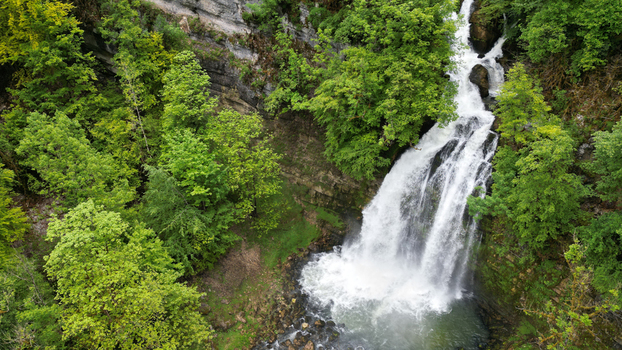 Aerial view of Cascades du Flumen waterfall cascading down a rocky cliff surrounded by lush green forest in Septmoncel Les Molunes Bourgogne Franche Comte France. Aerial view of Cascades du Flumen waterfall cascading down a rocky cliff surrounded by lush green forest in Septmoncel Les Molunes Bourgogne Franche Comte France.