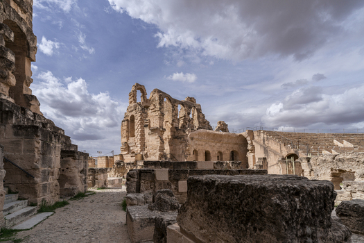 View of the ancient stone ruins of the Amphitheatre of El Jem under a cloudy sky in El Jem Gouvernorat de Mahdia Tunisia.