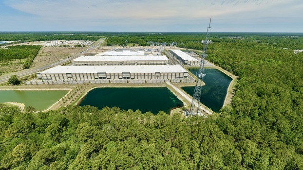 Aerial view of a large industrial warehouse complex and a tall communication tower next to retention ponds and dense green forest in World Golf Village Florida United States.
