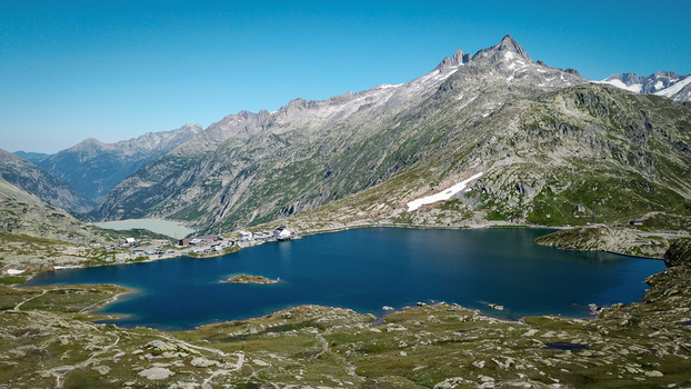 Aerial view of Grimsel Pass featuring the blue waters of Totensee lake surrounded by rugged alpine peaks and rocky terrain in Obergoms Valais Switzerland. Aerial view of Grimsel Pass featuring the blue waters of Totensee lake surrounded by rugged alpine peaks and rocky terrain in Obergoms Valais Switzerland.