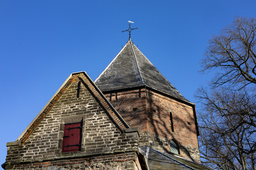 View of the historic Sint Nicolaaskapel featuring its brick facade pointed slate roof with a cross and a small red door under a clear blue sky in Nijmegen Gelderland Netherlands. View of the historic Sint Nicolaaskapel featuring its brick facade pointed slate roof with a cross and a small red door under a clear blue sky in Nijmegen Gelderland Netherlands.