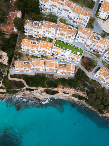 Aerial view of resort buildings with orange roofs and a green terrace overlooking the turquoise sea and rocky cliffs Cala Mendia Illes Balears Spain. Aerial view of resort buildings with orange roofs and a green terrace overlooking the turquoise sea and rocky cliffs Cala Mendia Illes Balears Spain.
