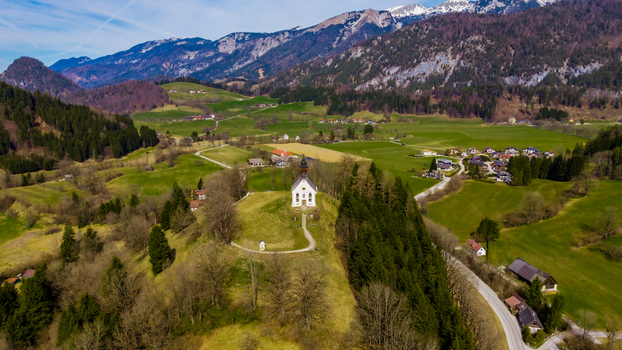 Aerial view of a pristine white church perched atop a hill contrasting against the lush green valley and snow capped mountains in the distance Windischgarsten Upper Austria Austria. Aerial view of a pristine white church perched atop a hill contrasting against the lush green valley and snow capped mountains in the distance Windischgarsten Upper Austria Austria.