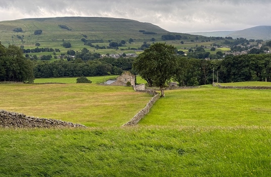 Yorkshire UK View of green pastures and dry stone walls with rolling hills and a stone barn under a cloudy sky. Yorkshire UK View of green pastures and dry stone walls with rolling hills and a stone barn under a cloudy sky.