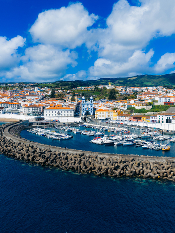 Aerial view of the historic harbor and the blue Igreja da Misericordia church surrounded by white buildings and green hills in Angra do Heroismo Azores Portugal.