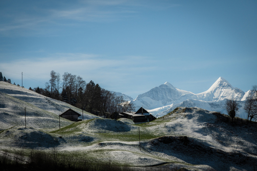 View of snow dusted hills cradle rustic wooden chalets beneath the watchful gaze of majestic snow capped peaks Train from Lucerne to Interlaken Switzerland. View of snow dusted hills cradle rustic wooden chalets beneath the watchful gaze of majestic snow capped peaks Train from Lucerne to Interlaken Switzerland.