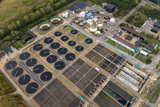 Aerial view of the water treatment plant featuring circular sedimentation tanks and rectangular aeration basins surrounded by industrial buildings and greenery in Broughton England United Kingdom. Aerial view of the water treatment plant featuring circular sedimentation tanks and rectangular aeration basins surrounded by industrial buildings and greenery in Broughton England United Kingdom.