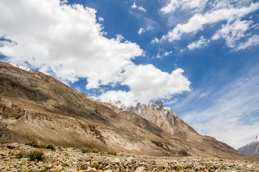 View of the rugged mountain landscape near K2 Base Camp with rocky slopes sparse vegetation and a bright blue sky with scattered white clouds in Gilgit Pakistan. View of the rugged mountain landscape near K2 Base Camp with rocky slopes sparse vegetation and a bright blue sky with scattered white clouds in Gilgit Pakistan.