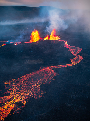 Aerial view of a volcanic eruption with glowing lava fountains and a flowing river of molten rock across the dark volcanic landscape in Iceland. Aerial view of a volcanic eruption with glowing lava fountains and a flowing river of molten rock across the dark volcanic landscape in Iceland.